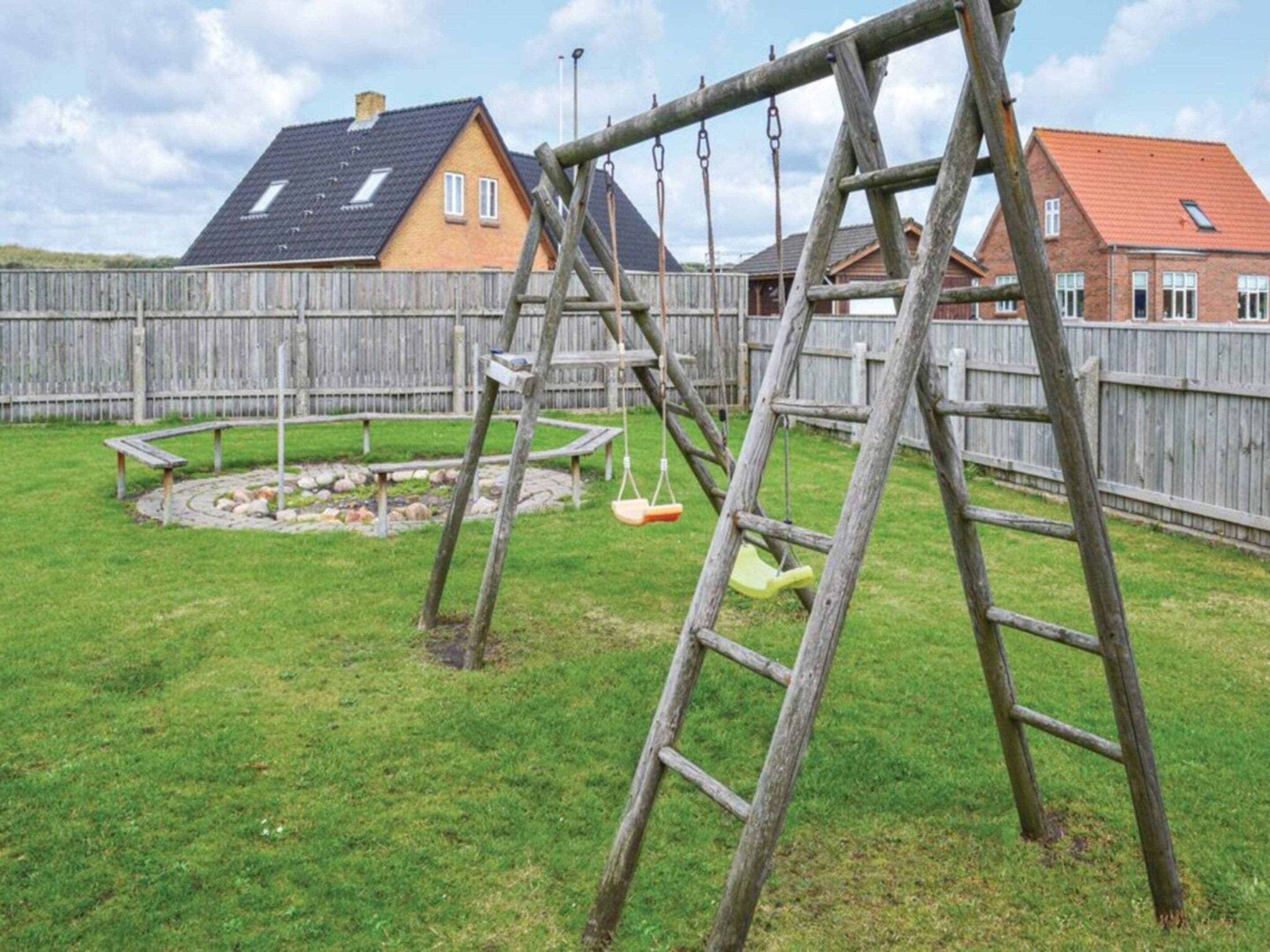 A backyard with a wooden swing set, a small circular play area, and a wooden fence.