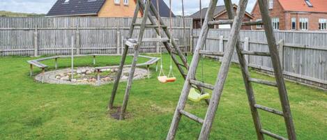 A backyard with a wooden swing set, a small circular play area, and a wooden fence.