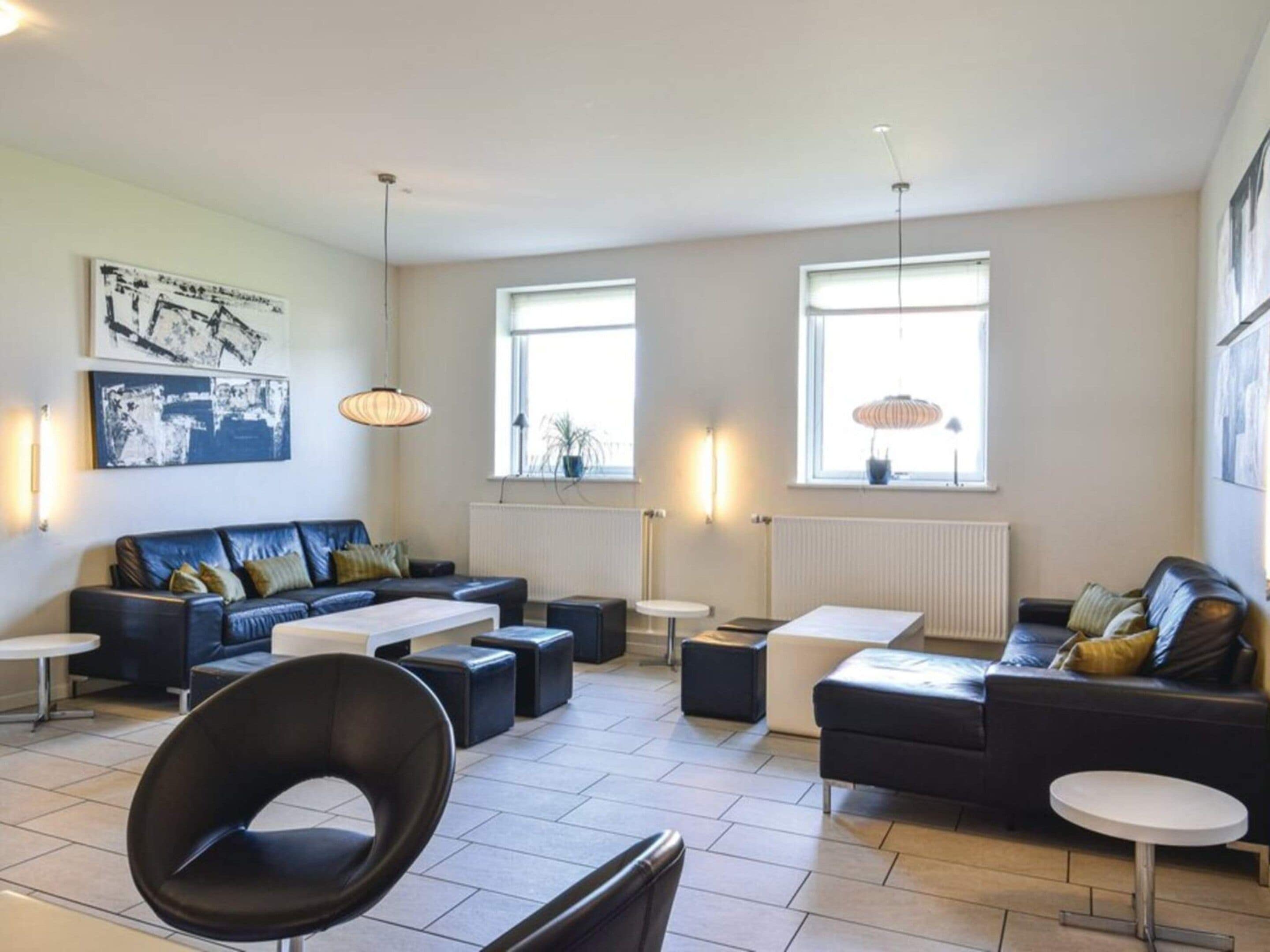 A modern living room with a sofa set, a coffee table, and a chair. There are two windows providing natural light.