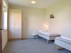 A room with two single beds, a small round table, a wardrobe, and a wall-mounted light fixture. - 4 Star Holiday Home in Thyboron (Thyborøn)