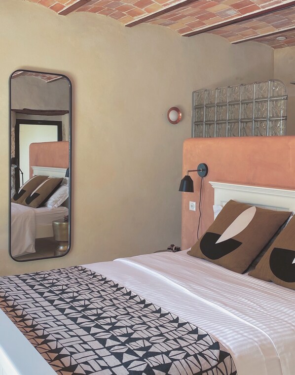 Una habitación de hotel con una cama, un espejo grande, un cabecero y una colcha estampada.