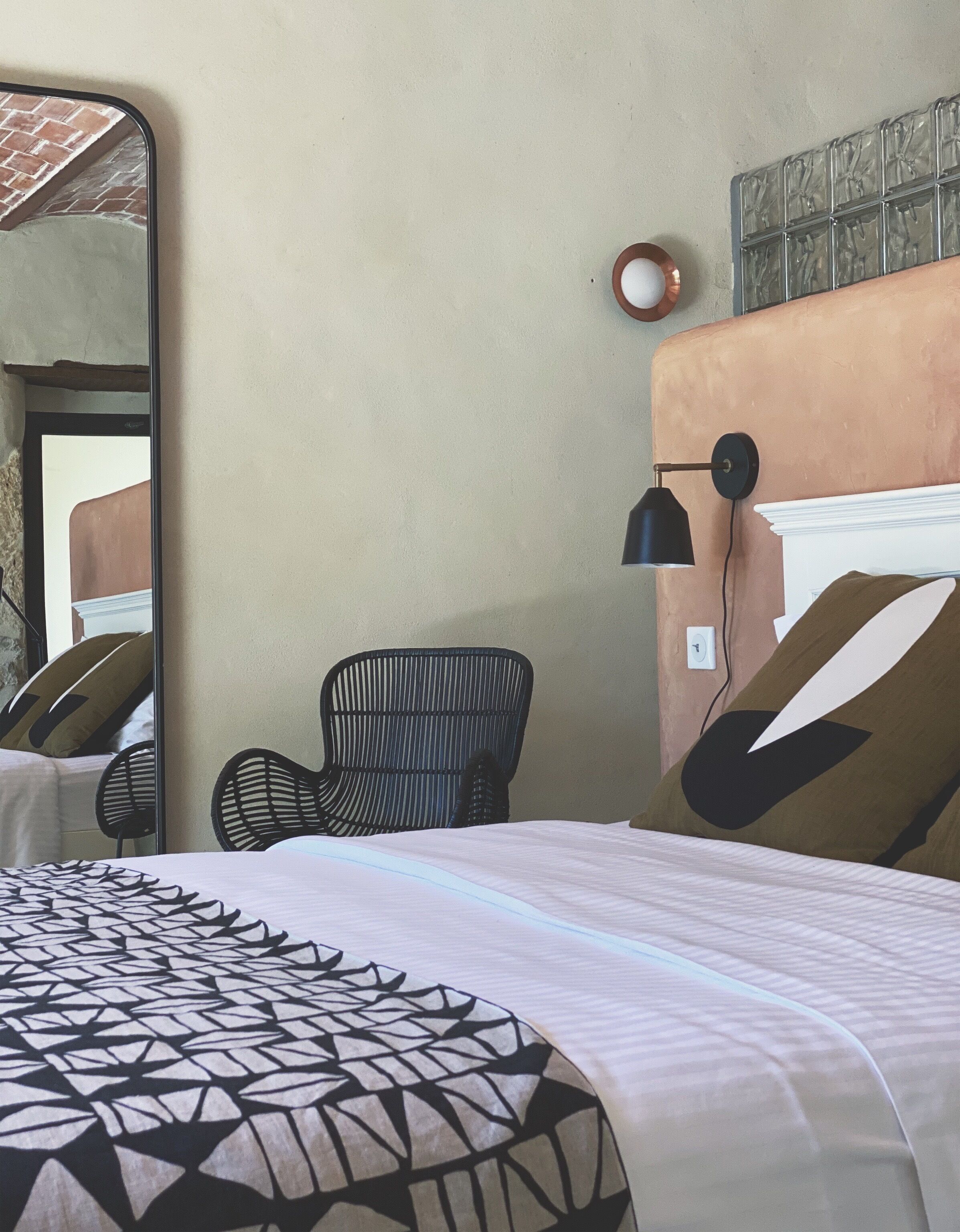 A hotel room with a bed, a chair, a lamp, and a mirror.