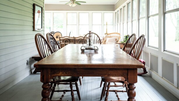 A dining room with a wooden table and chairs, large windows, and a ceiling fan. - Farmhouse With Heated Pool on Almost 160 Acres! (Elkhorn)