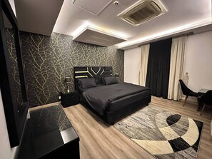 Quarto moderno com parede estampada em preto e dourado, uma cama grande com cabeceira geométrica, uma mesa de cabeceira e um tapete circular.
