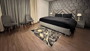 Ein modernes Hotelzimmer mit einem großen Bett, zwei Sesseln, einem kleinen Tisch und einem Teppich mit geometrischem Muster.