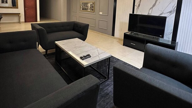 Ein modernes Wohnzimmer mit einer Sofagarnitur, einem Couchtisch, einem Fernseher und einer Wand mit Marmorverkleidung.