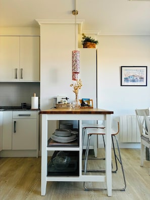 A modern kitchen with white cabinets, a wooden table, and a hanging plant.