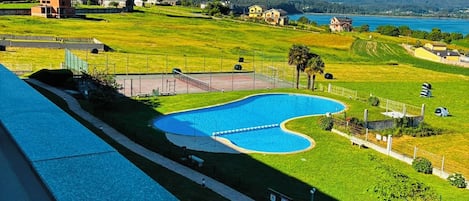 Una piscina de forma singular, rodeada por un césped cuidado y con vistas despejadas al mar y montañas distantes.