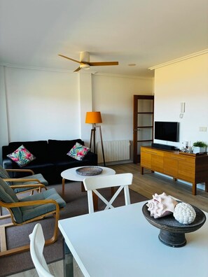 A modern living room with a sofa, chairs, a small table, a lamp, a TV, and a cabinet.