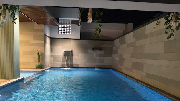 Piscina interna con cascata, pareti piastrellate e piante in vaso.