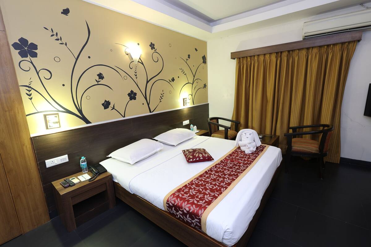 A hotel room with a large bed, bedside tables, a chair, and a decorative wall with floral patterns.