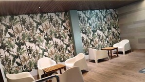 Un'area lounge moderna con sedie bianche, un tavolo in legno e carta da parati con motivi tropicali.