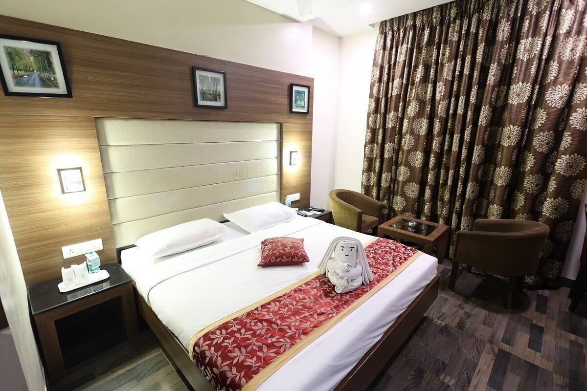 A hotel room with a bed, a nightstand, a chair, and a large window with curtains.