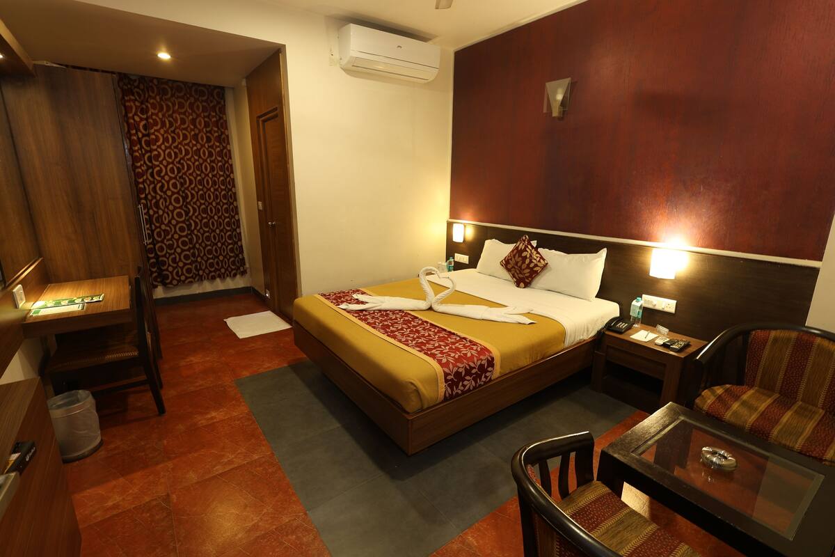 A hotel room with a bed, a desk, a chair, a table, and a nightstand.