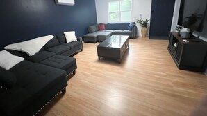 Un salon avec un mur bleu foncé, un plancher en bois, un canapé d’angle, une table basse et un téléviseur posé sur un meuble.