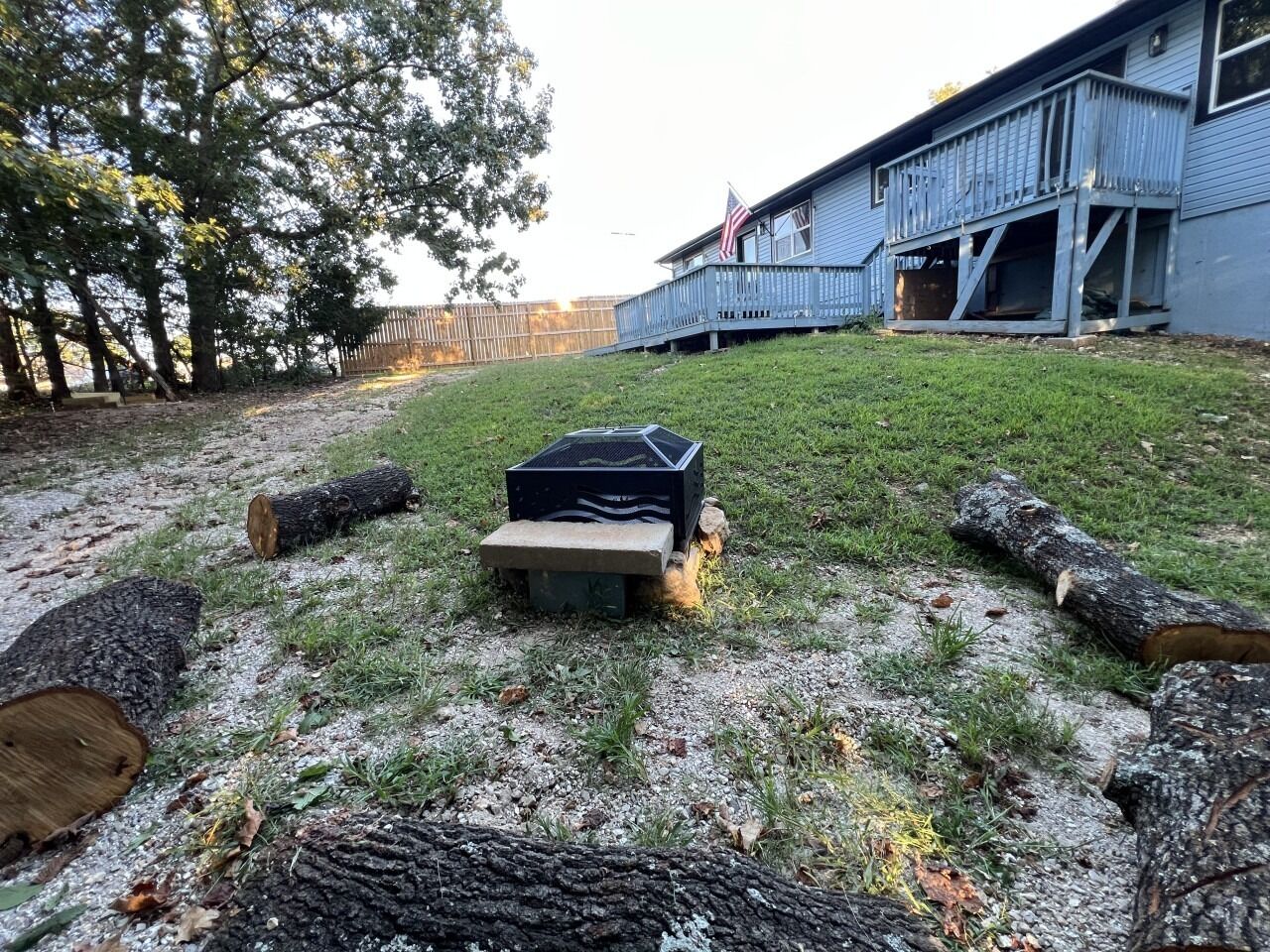 A backyard with a wooden deck, a metal grill, and logs.