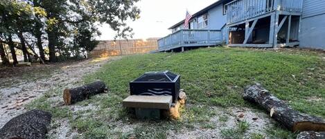 A backyard with a wooden deck, a metal grill, and logs.