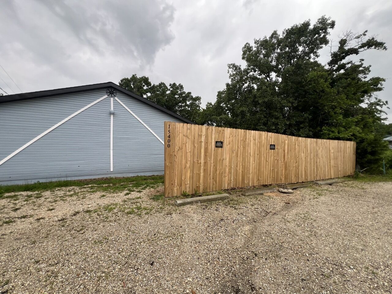 Une allée de gravier mène à une clôture en bois et à un bâtiment en métal.