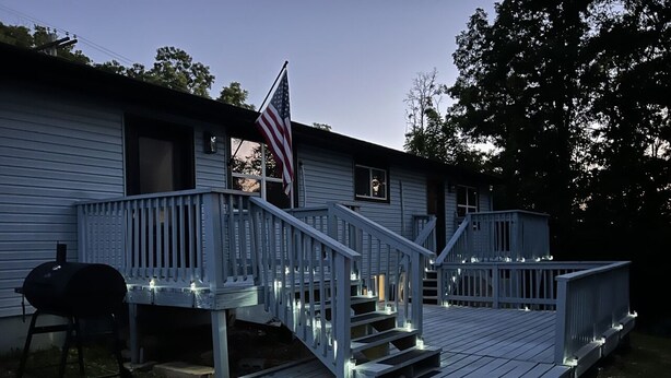 Une maison avec une terrasse en bois, un barbecue et un drapeau américain.