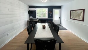 Un espace repas avec une longue table, des chaises noires et une nappe blanche.