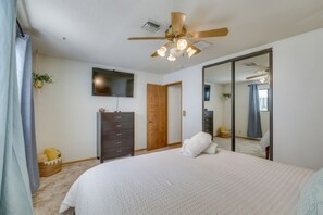 Ein Schlafzimmer mit Bett, Deckenventilator, Fernseher, Kleiderschrank und Spiegel.