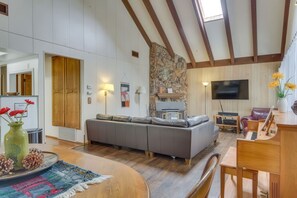 Una sala moderna con un sofá seccional gris, una mesa de comedor de madera y un piano.