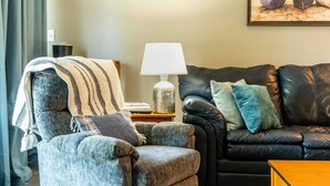 A living room with a leather sofa, a grey armchair, a lamp, and a painting of boats on the wall. - Cozy Condo at Interlaken! Stay & Play on Lake Como (Lake Geneva)