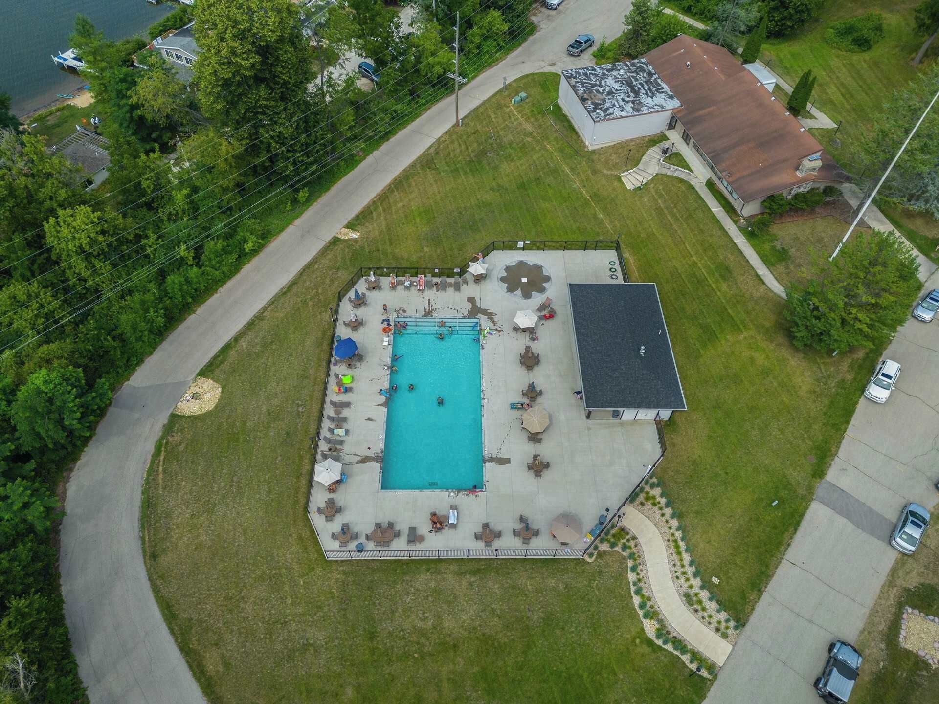 An aerial view of a residential area with a swimming pool, a covered patio, and a detached garage.