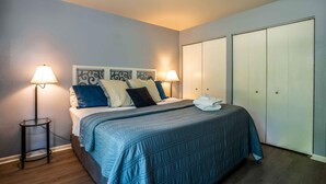 A neatly made bed with a blue quilt, two bedside lamps, and a large wardrobe. - Cozy Condo at Interlaken! Stay & Play on Lake Como (Lake Geneva)