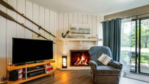 A living room with a fireplace, a television on a wooden stand, and a comfortable armchair. - Cozy Condo at Interlaken! Stay & Play on Lake Como (Lake Geneva)