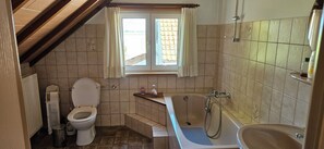 A bathroom with a toilet, bathtub, and window.