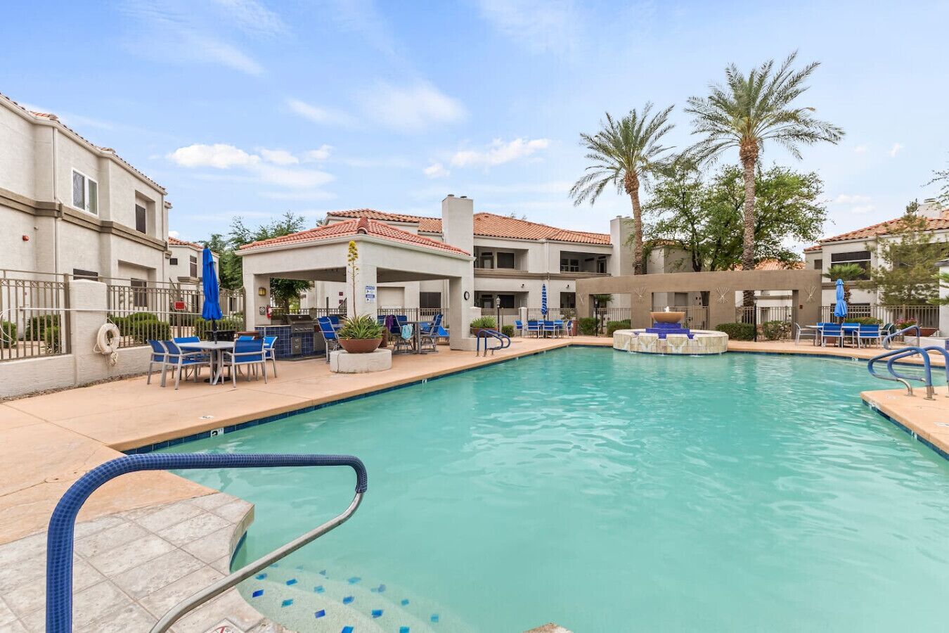 A swimming pool with lounge chairs and umbrellas, surrounded by buildings with a tiled roof.