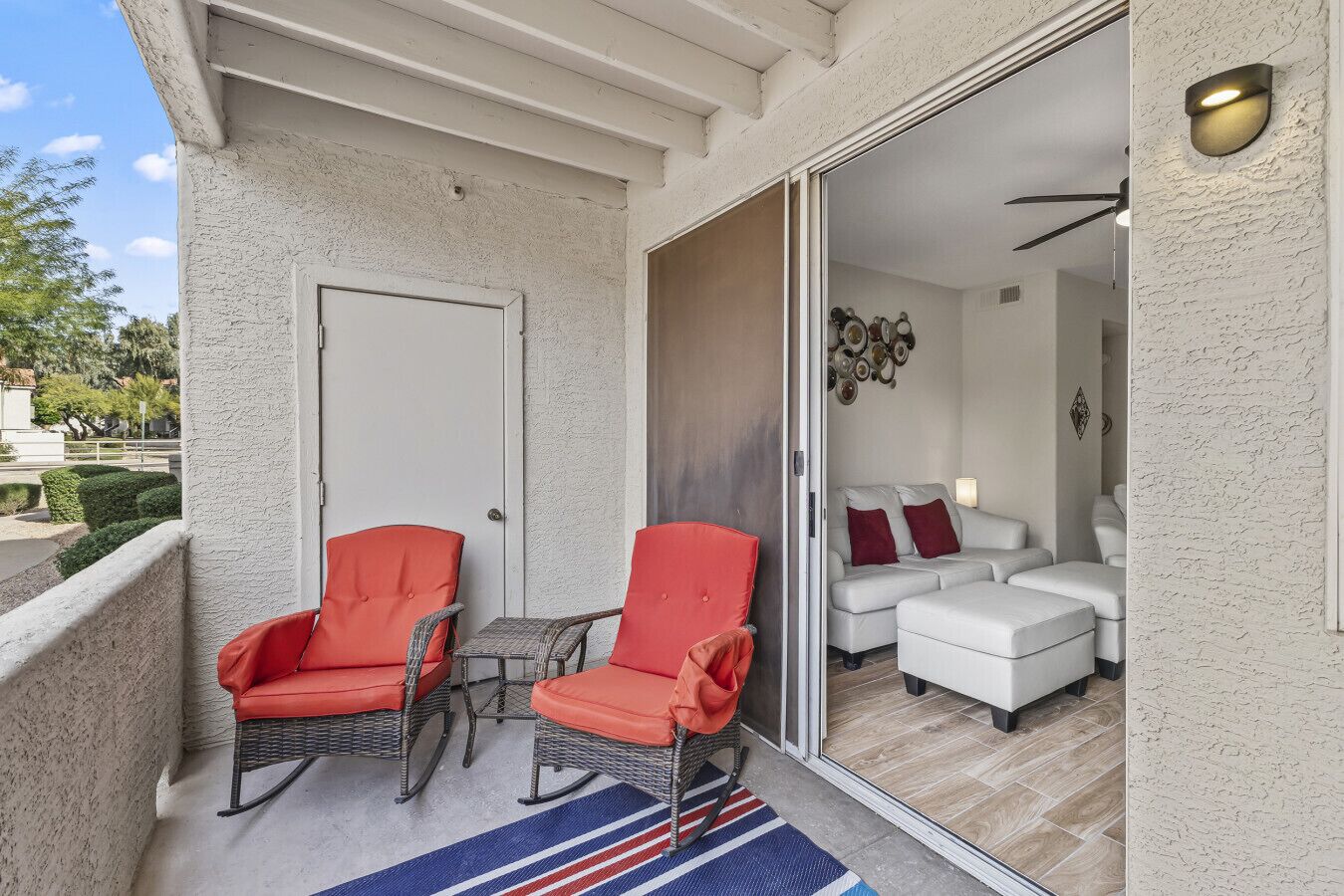 A balcony with wicker chairs, a small table, and a striped rug.