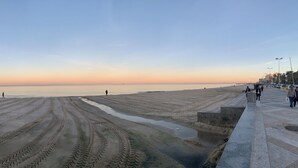 A wide promenade with a clear view of the sea, a sandy beach with tire tracks, and a distant shoreline. - Bel Appartement (Sousse)