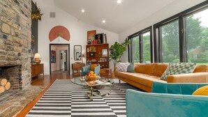 Una sala de estar moderna con chimenea de piedra, un ventanal grande y una combinación de muebles contemporáneos y clásicos.