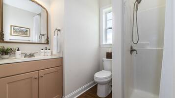 A bathroom with a beige vanity, a large mirror, a toilet, and a shower.