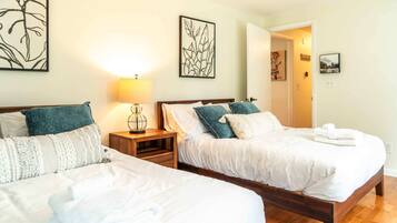 A hotel room with two beds, a bedside table with a lamp, and artwork on the walls.
