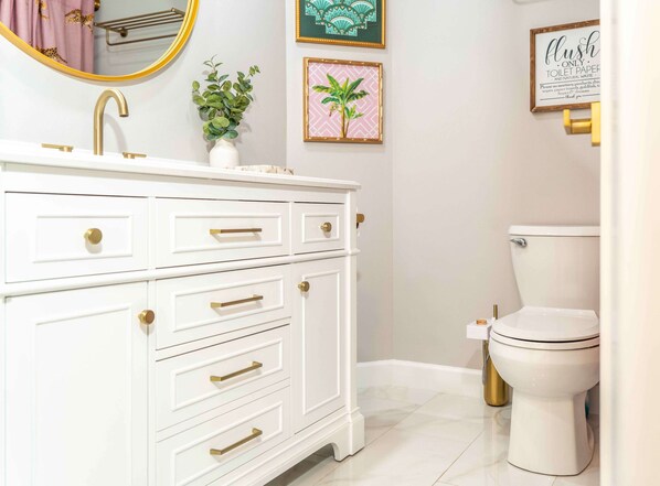 Et hvidt toiletbord med guldgreb, en guldfarmet vandhane og en potteplante.