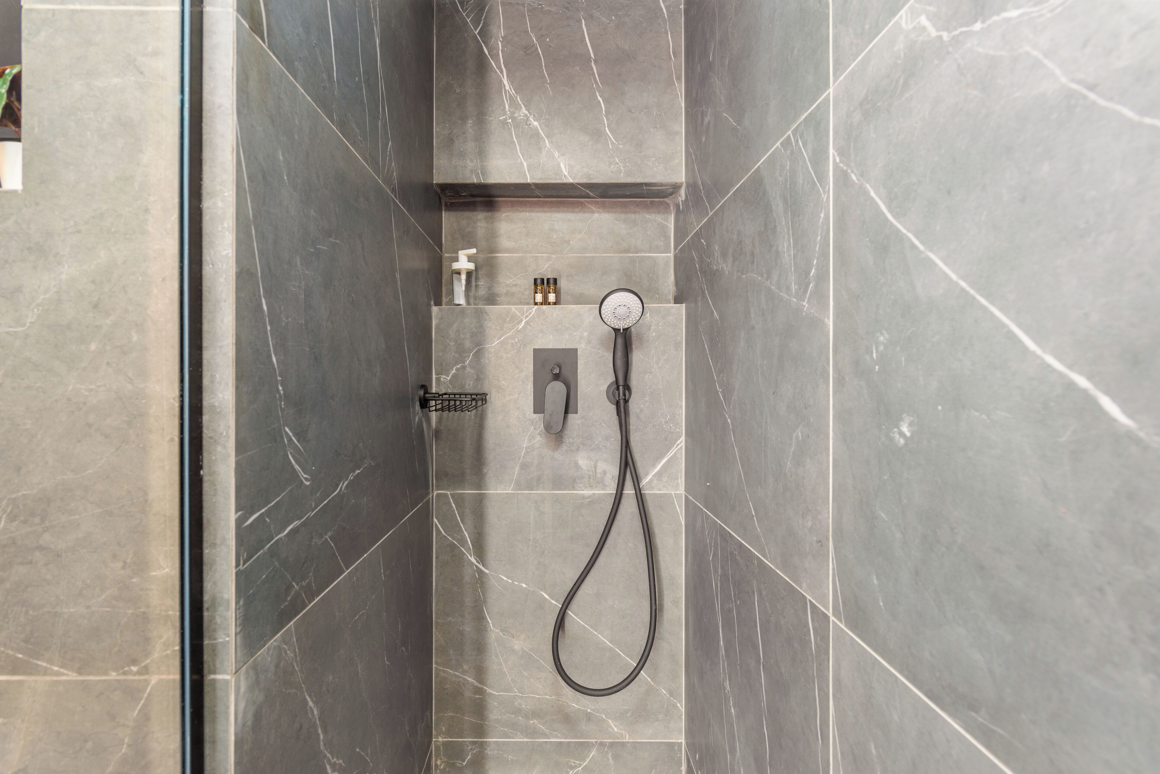 A modern shower area with a handheld showerhead, a control panel, and a soap dispenser.