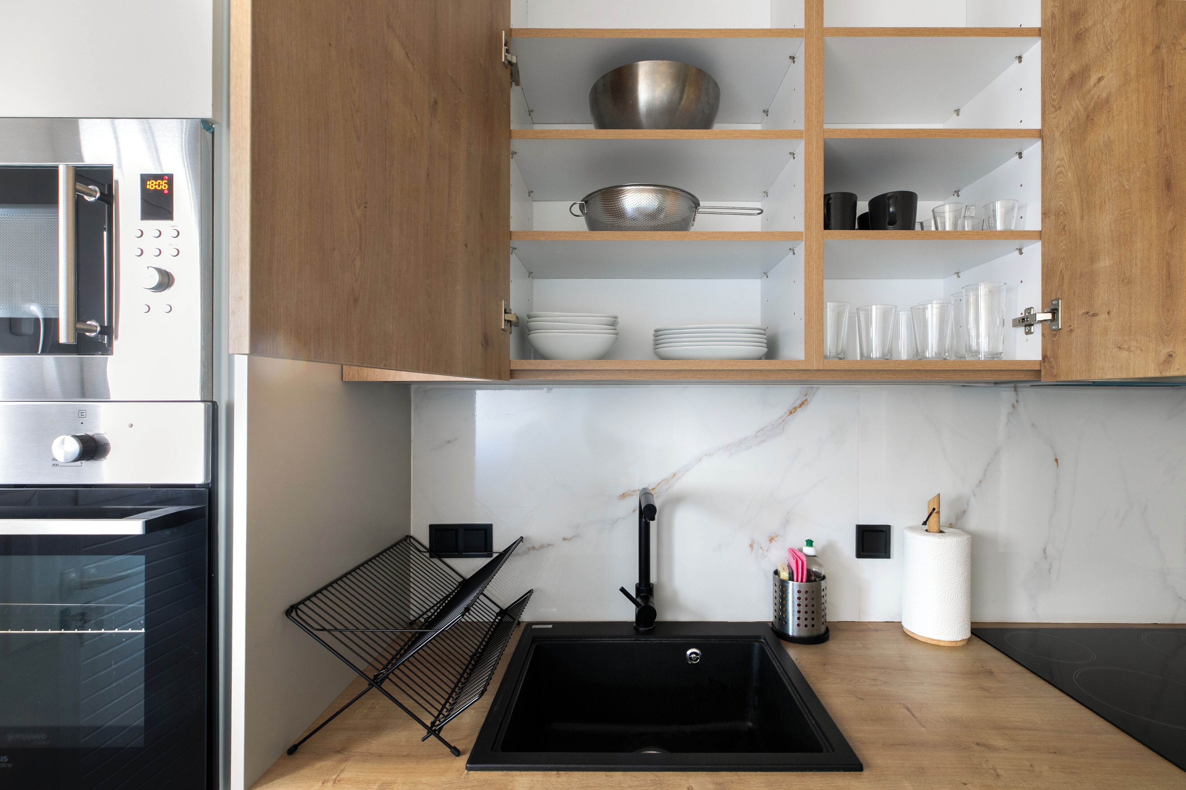 A kitchen with a built-in oven, a black sink, wooden cabinets, and a marble backsplash.