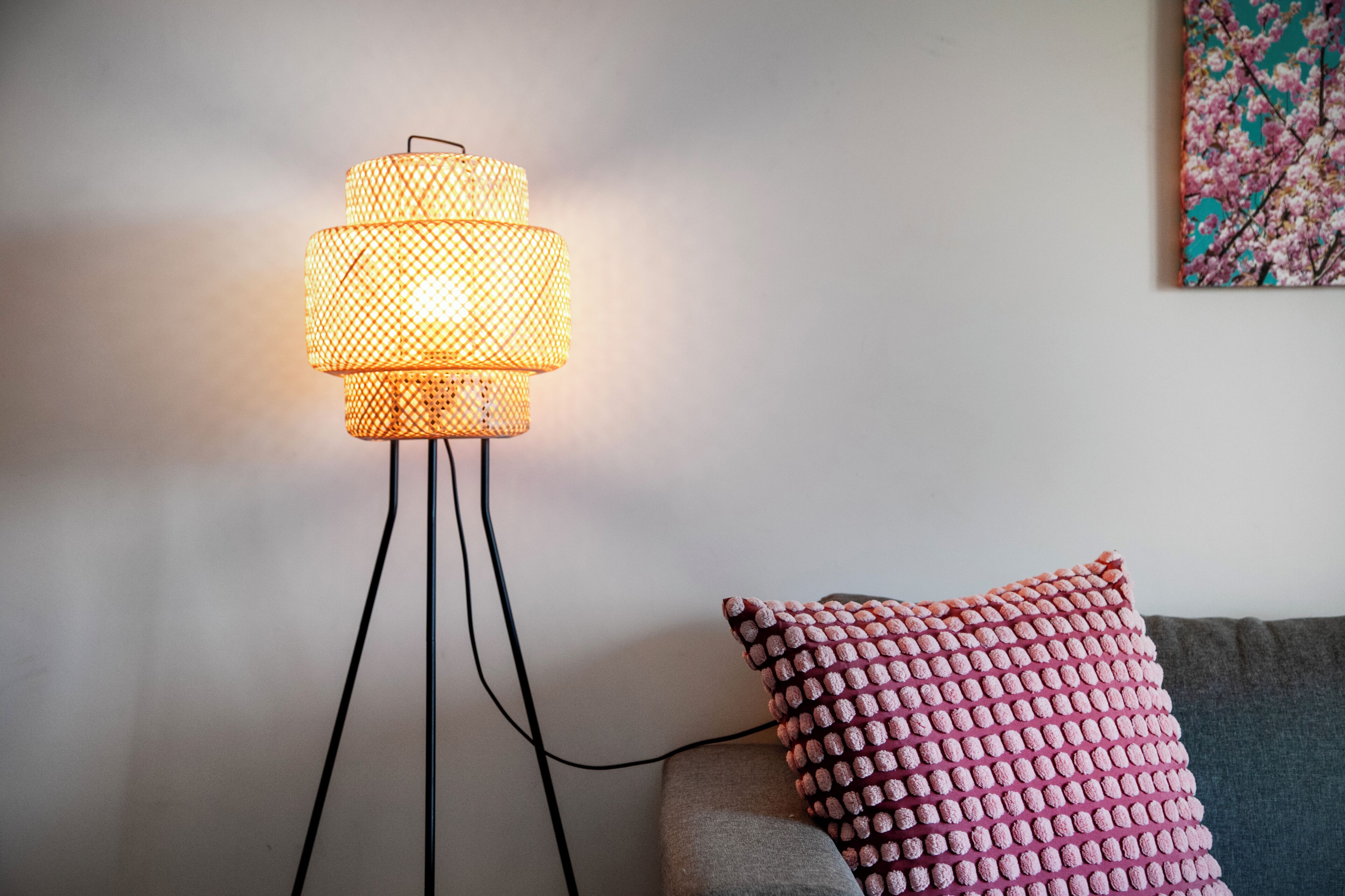 A floor lamp with a woven shade, a grey sofa, and a patterned cushion.