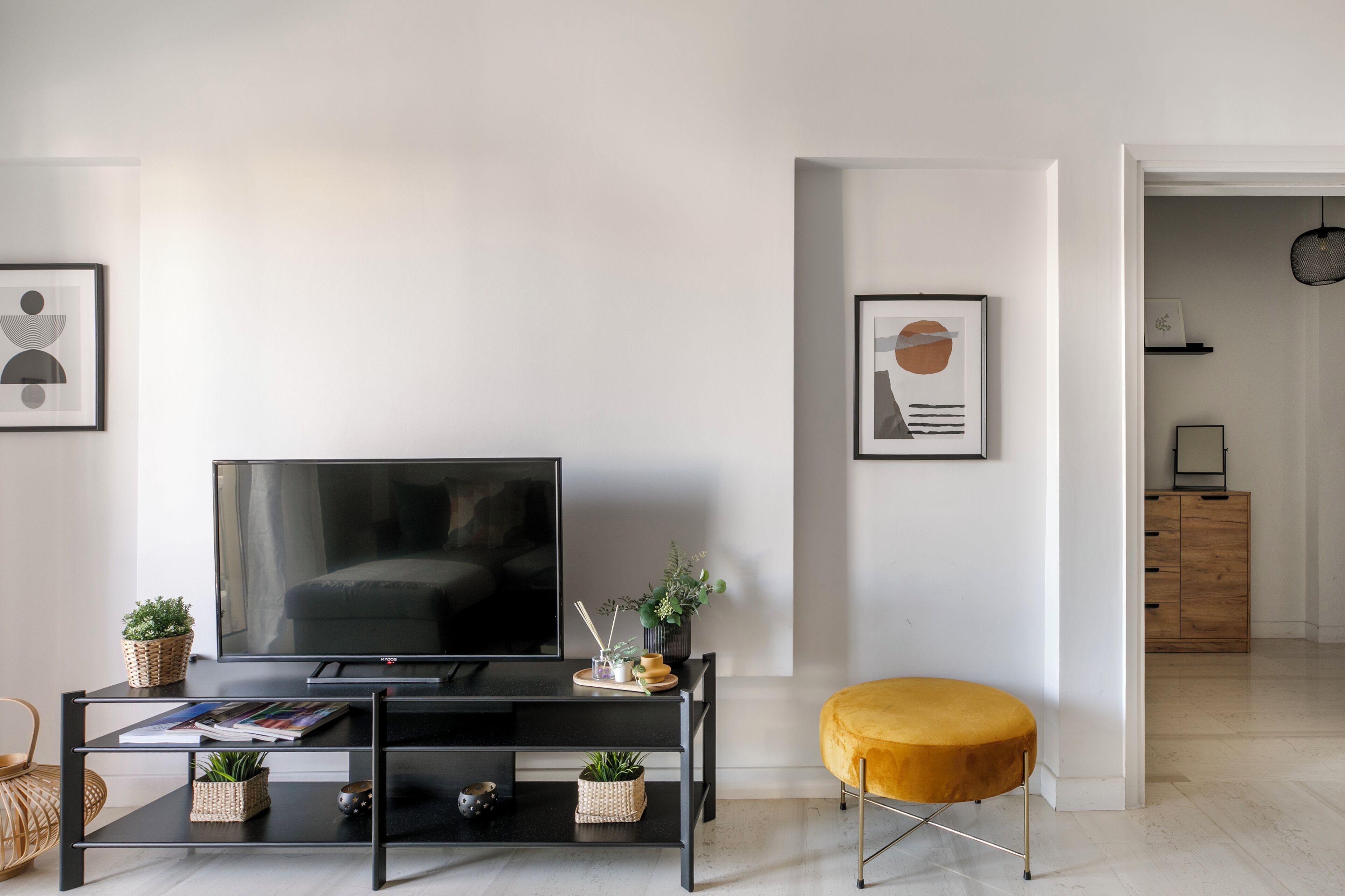 Un soggiorno moderno con una grande TV a schermo piatto su un supporto nero, un poggiapiedi giallo e un tavolino da caffè nero con riviste e piccole piante.