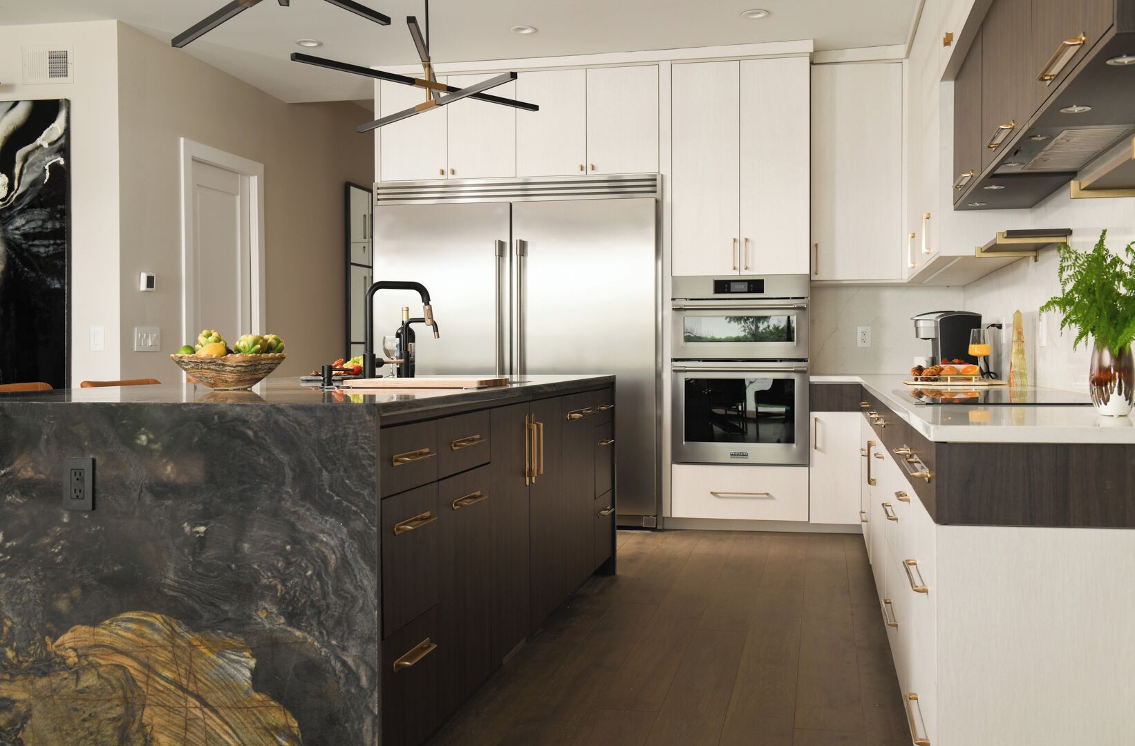 A modern kitchen with dark cabinetry, stainless steel appliances, and a marble island.