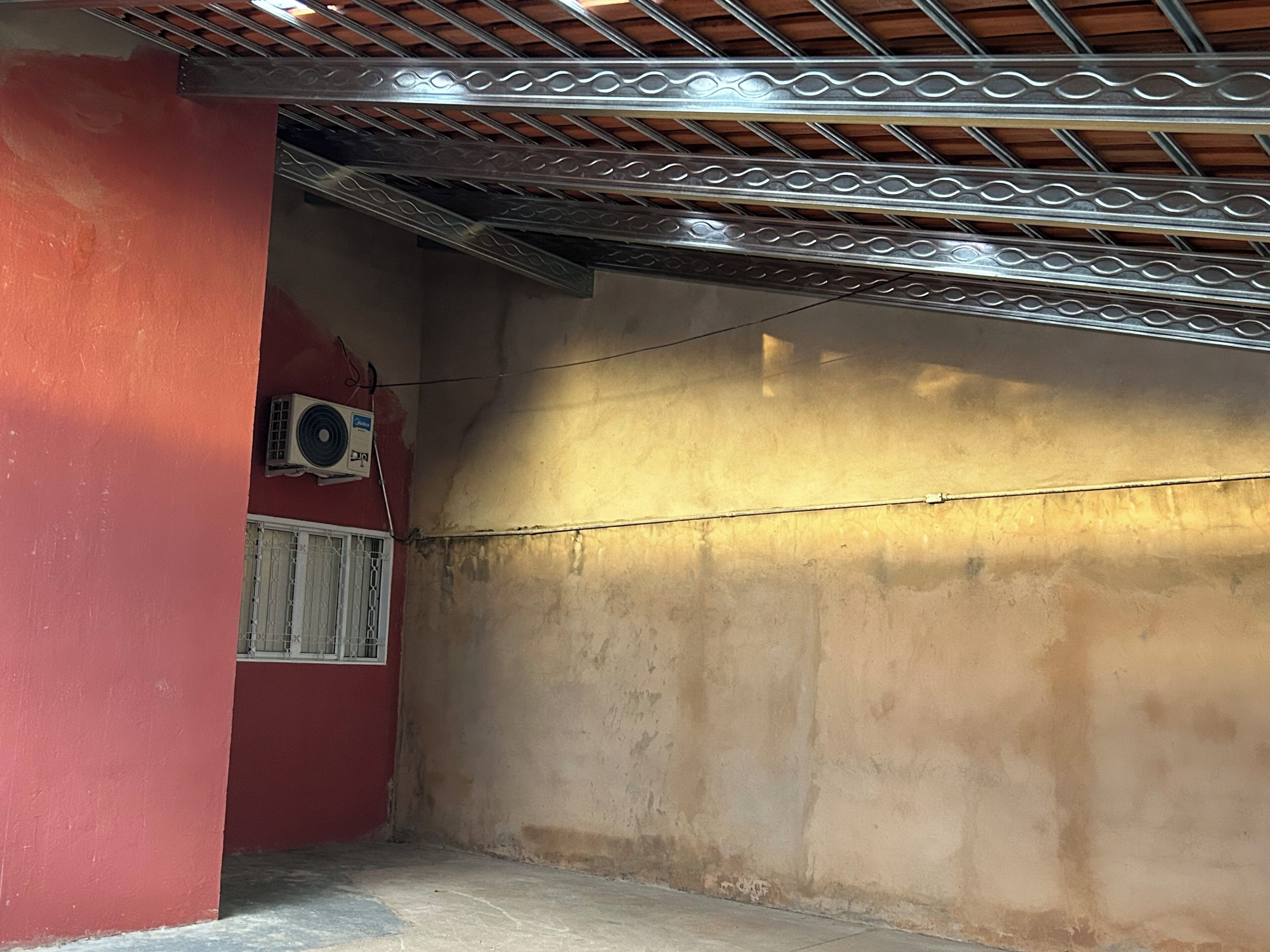 Une pièce avec un mur rouge, un plafond en métal et une fenêtre ornée d’une grille blanche.