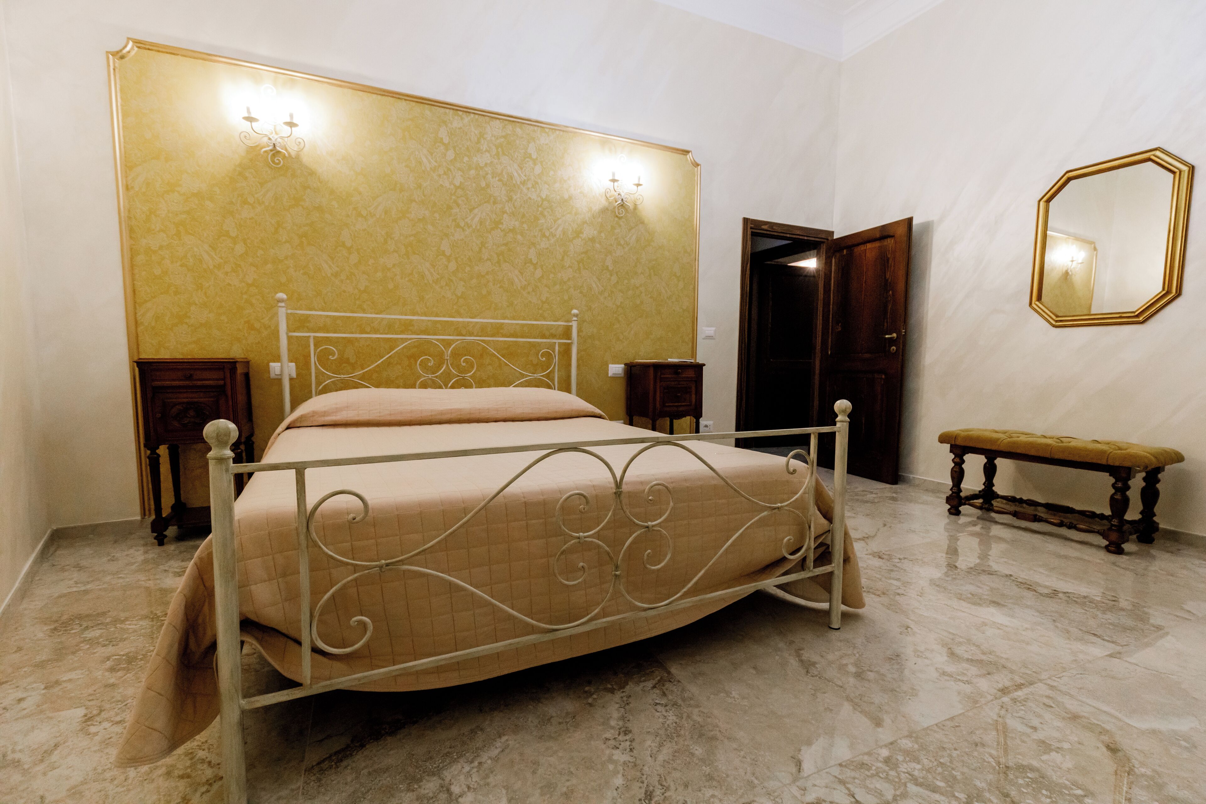 A neatly arranged bedroom with a metal-framed bed, a wooden bench, a mirror, and a door.