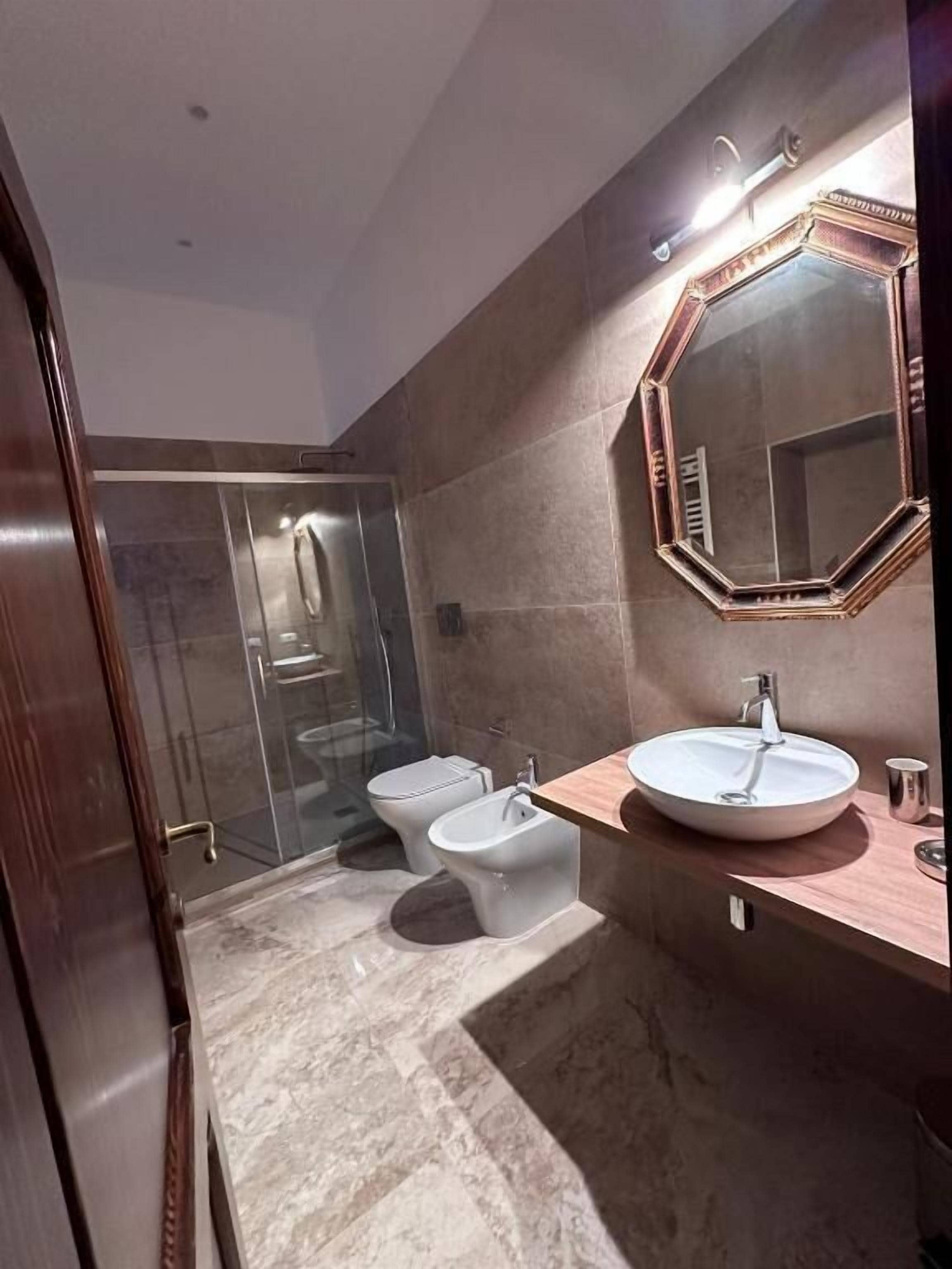 A modern bathroom with a large mirror, two toilets, a bidet, and a shower area.