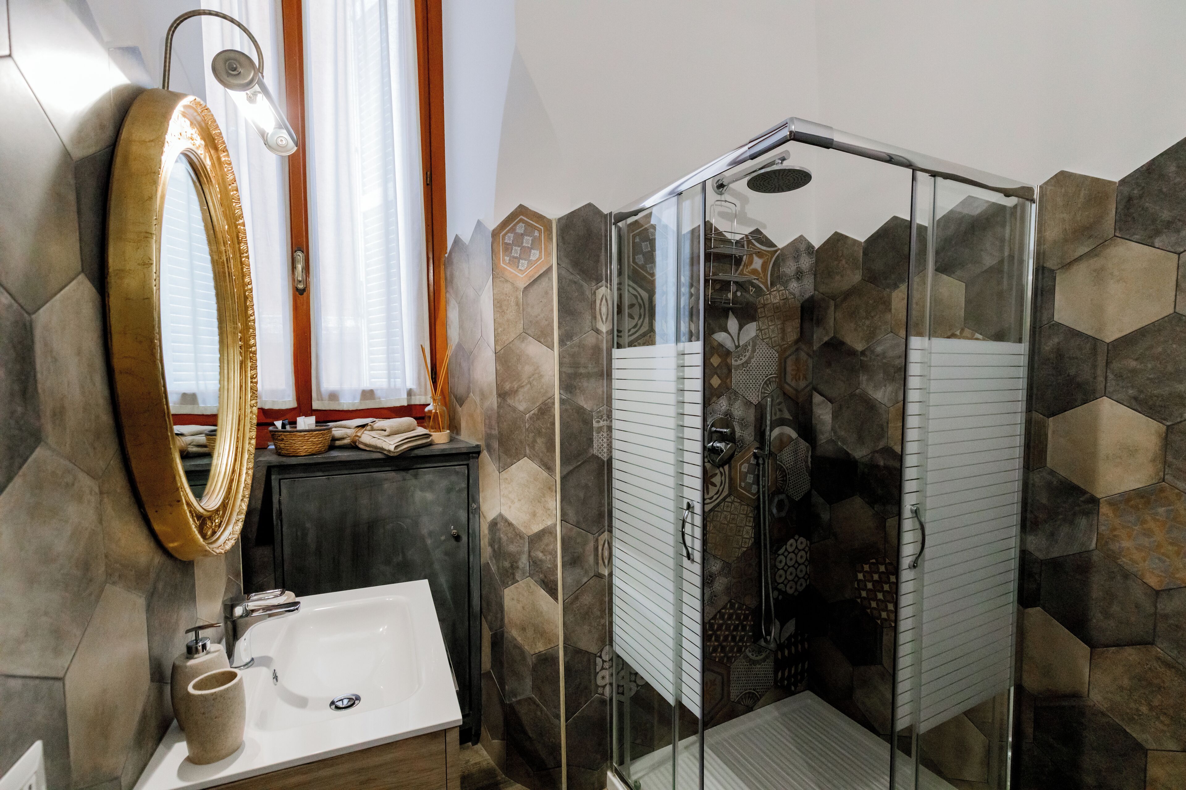 A bathroom with a glass-enclosed shower, a large mirror, and a sink with a soap dispenser.