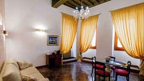 A room with a sofa, dining table, chairs, a chandelier, and curtains.