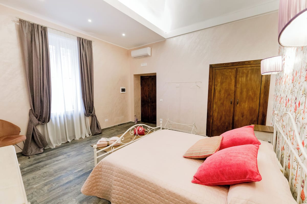 A bedroom with a bed, a wardrobe, a window with curtains, and a hanging light fixture.