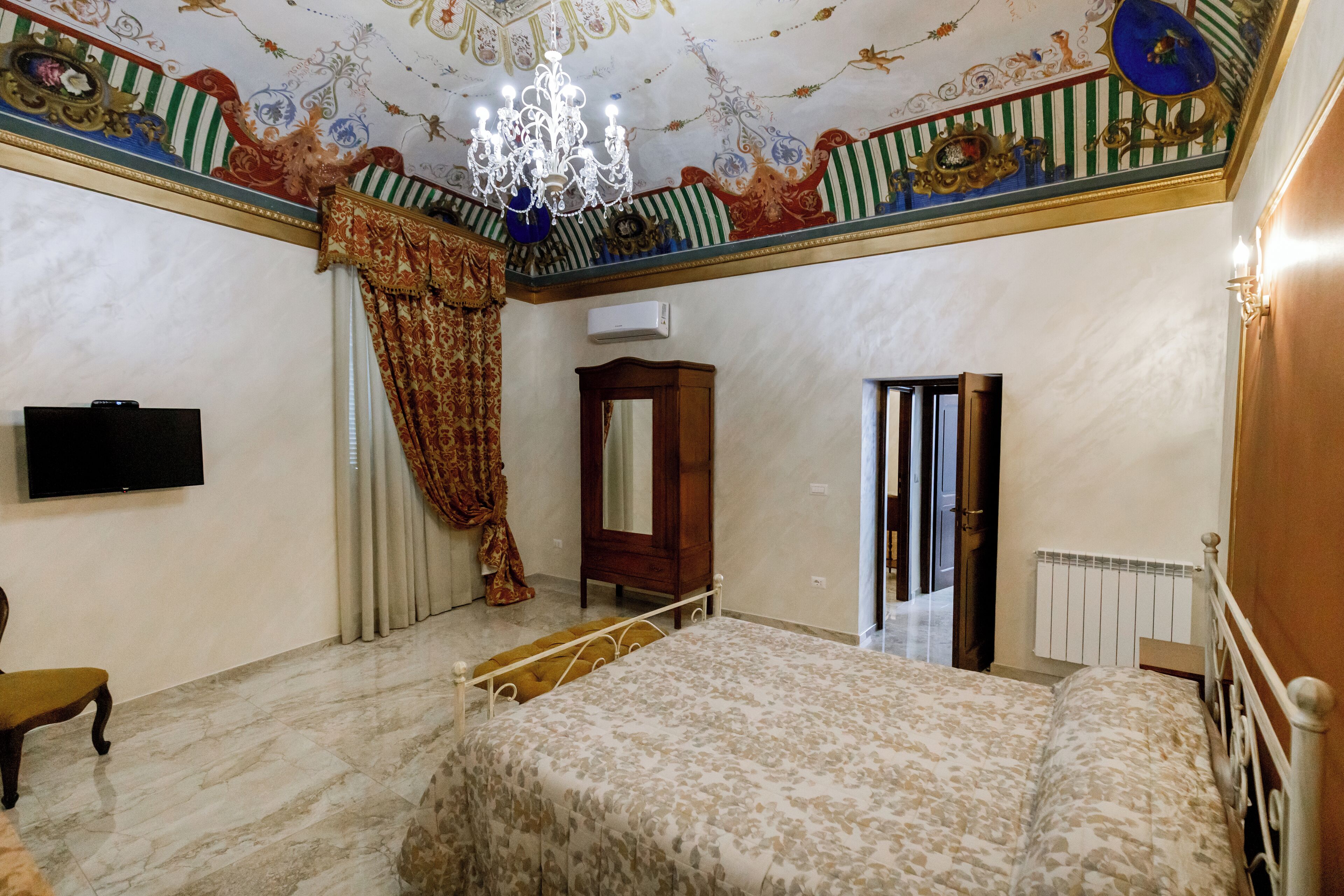 A bedroom with a bed, a television, a mirror, and a chandelier.